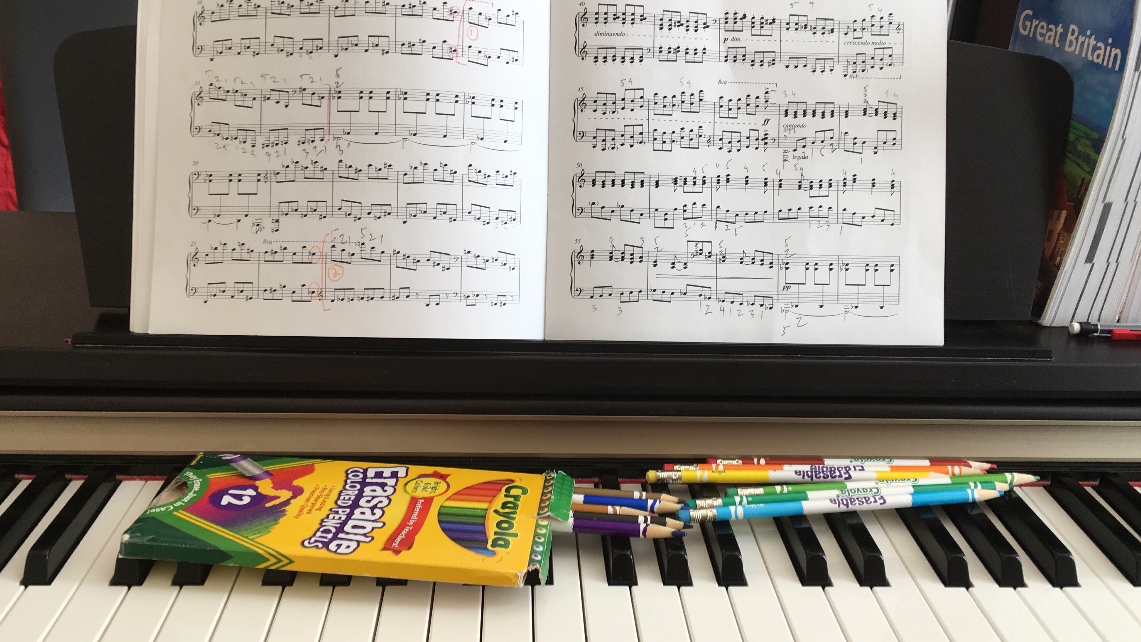 Crayola colored pencils resting on piano keys beside an open sheet music book, evoking the joy of learning music