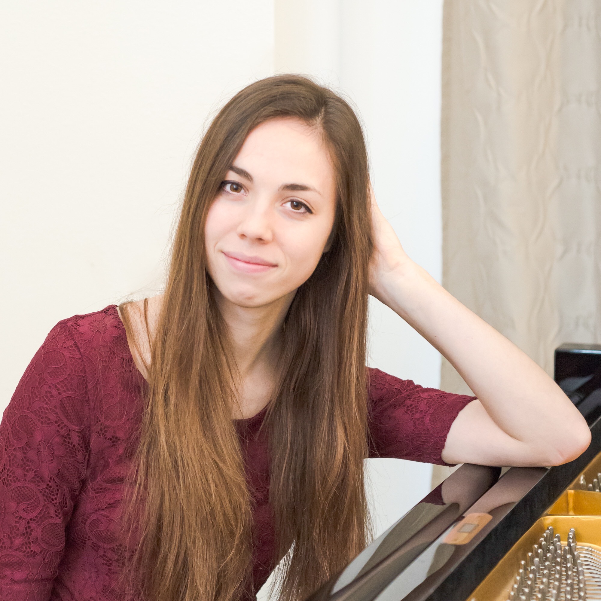 Kristianna Callahan smiling at the camera while leaning on an open piano, wearing a red lace top